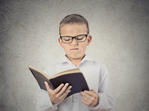 Unhappy Boy Reading Book, isolated on grey wall background 