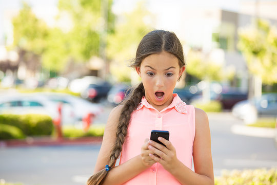 Shocked child texting on mobile, smart phone, outside background