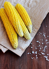 Boiled corn with sea salt on the parchment, wooden background, v