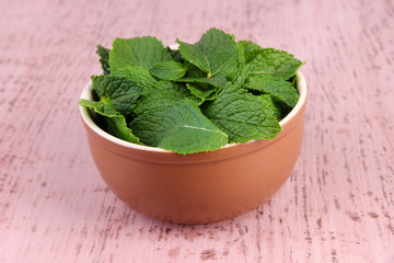 Brown round bowl of fresh mint leaves on pink wooden background