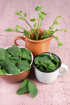 Brown round bowl and white metal mug of fresh mint leaves and