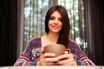 Happy beautiful woman sitting at the table with cup of coffee