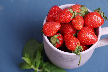 Ripe sweet strawberries in mug  on color wooden background