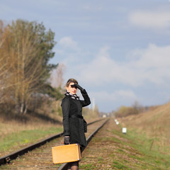 Woman with an old suitcase walking along railway sleepers