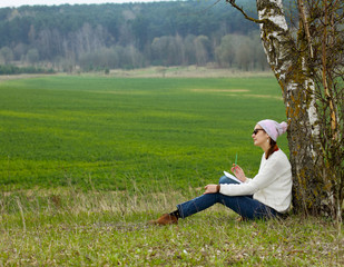 Ordinary hipster girl writing in a notebook outdoors