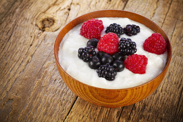 Yogurt with forest berries in wooden bowl