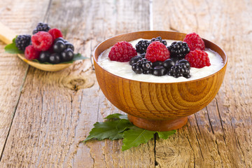Yogurt with wild berries in wooden bowl