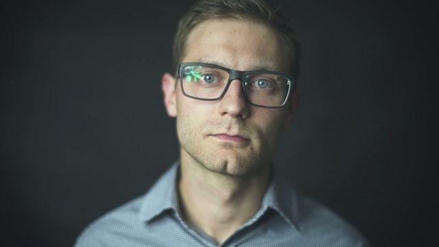 Handsome man in shirt putting on glasses over black background