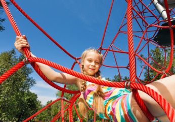 Girl with two braids sits on ropes of red net