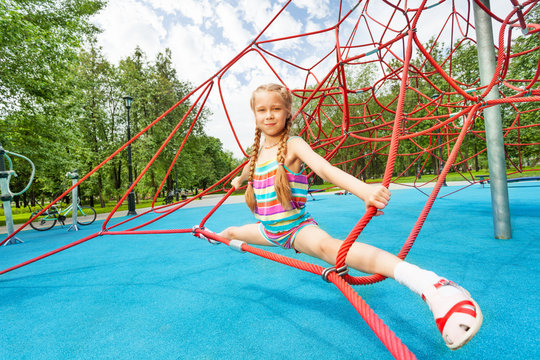 Active girl sits on red ropes in leg-split