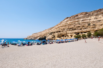 Fototapeta premium Tourists on Matala beach with the caves on Libyan sea, Greece.