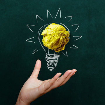 hand holding crumpled paper with Light bulb on blackboard backgr