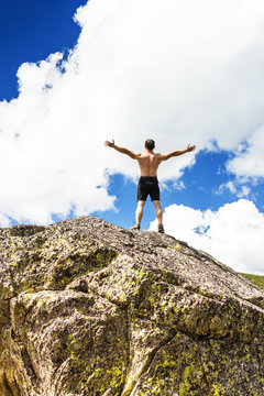 Young man standing on top of a cliff with arms raised
