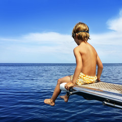 Boy sitting on boat bridge looking at the sea