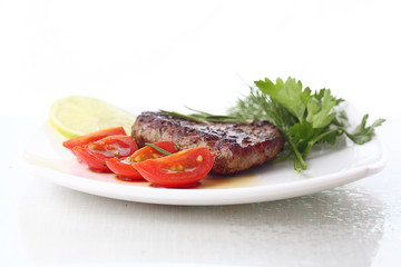 serving of meat with vegetables on a plate of white background