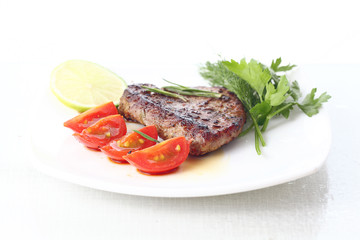 serving of meat with vegetables on a plate of white background