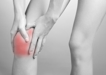 Pain concept. Woman holding sore knee in shades of grey