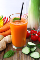 Glass of fresh carrot juice and vegetables on wooden table