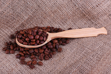 Wooden spoon of coffee beans on sacking background closeup