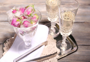 Ice cubes with rose flowers in glass bowl and two glasses with