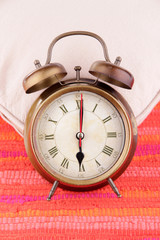 Metal clock on a white pillow on red background