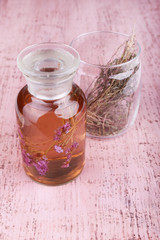 Bottle of tincture and glass of herbs on pink wooden background