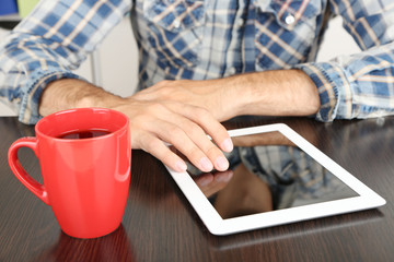 Man sitting on wooden table and working on tablet closeup