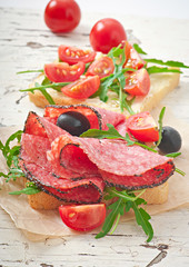 Sandwich with sausage, olive, tomato and arugula 