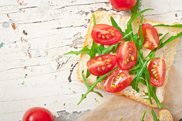Sandwich with tomato and arugula on the old wooden background