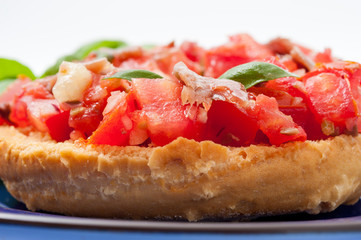 Frisella con pomodori rossi e acciughe su un piatto blu
