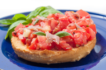 Frisella con pomodori rossi e acciughe su un piatto blu