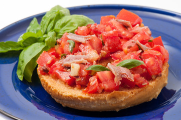 Frisella con pomodori rossi e acciughe su un piatto blu
