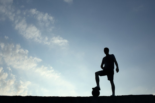 Silhouette of soccer man resting with foot on ball