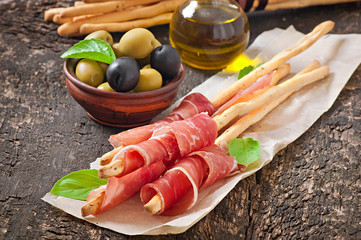 Grissini bread sticks with ham, olives, basil on table