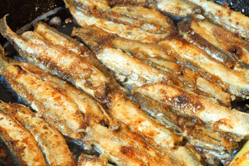 fried fish capelin on black frying pan