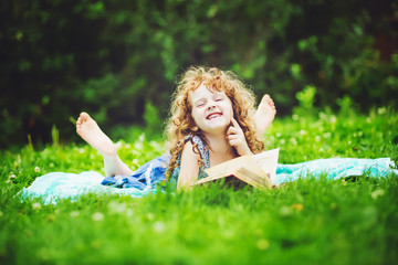 Little girl reading a book in the summer park, toning photo.