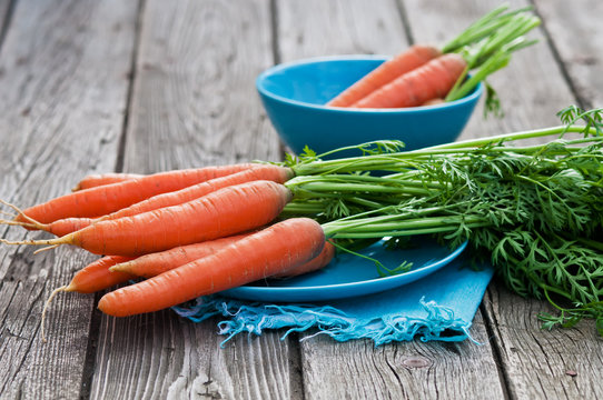 Fresh carrots on wooden background with blue napkin and plate