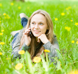 girl lying on grass with dandelions and talking on the phone