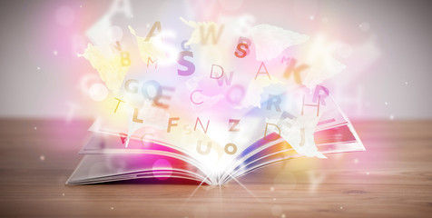 Open book with glowing letters on concrete background