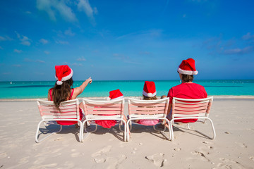 Happy family of four on beach in red Santa hats