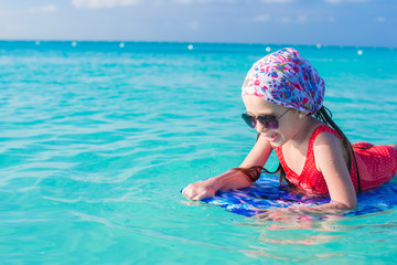 Little cute girl swimming on a surfboard in the turquoise sea