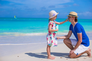 Little girl rubs sunscreen on nose of her dad