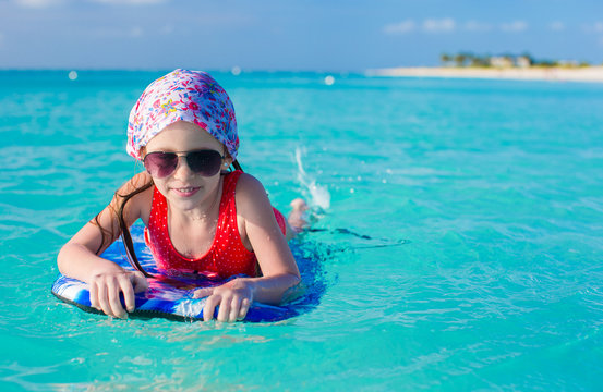 Little adorable girl on a surfboard in the turquoise sea