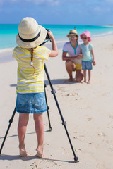 Little girl making photo of her dad and sister at the beach