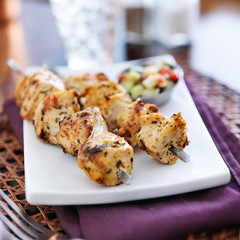 two grilled chicken skewers with cucumber salad