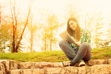 Young woman with tablet sitting in park laughing