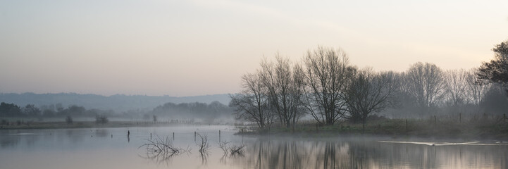 Panorama landscape of lake in mist with sun glow at sunrise