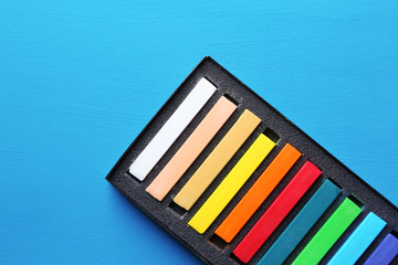 Colorful chalk pastels in box on color wooden background
