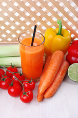 Glass of fresh carrot juice and vegetables on wooden table