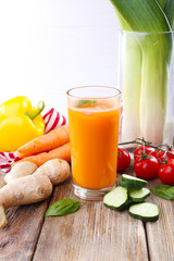 Glass of fresh carrot juice and vegetables on wooden table